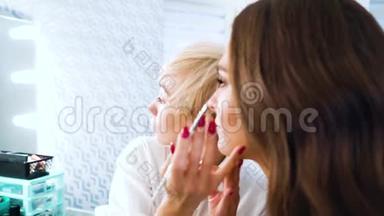 美妆师在美容院用刷子将唇彩涂在年轻女子脸上